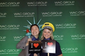 Zwei Mitarbeiter posieren mit Accessoires vor Fotobox Branding Hintergrund auf Corporate Event.