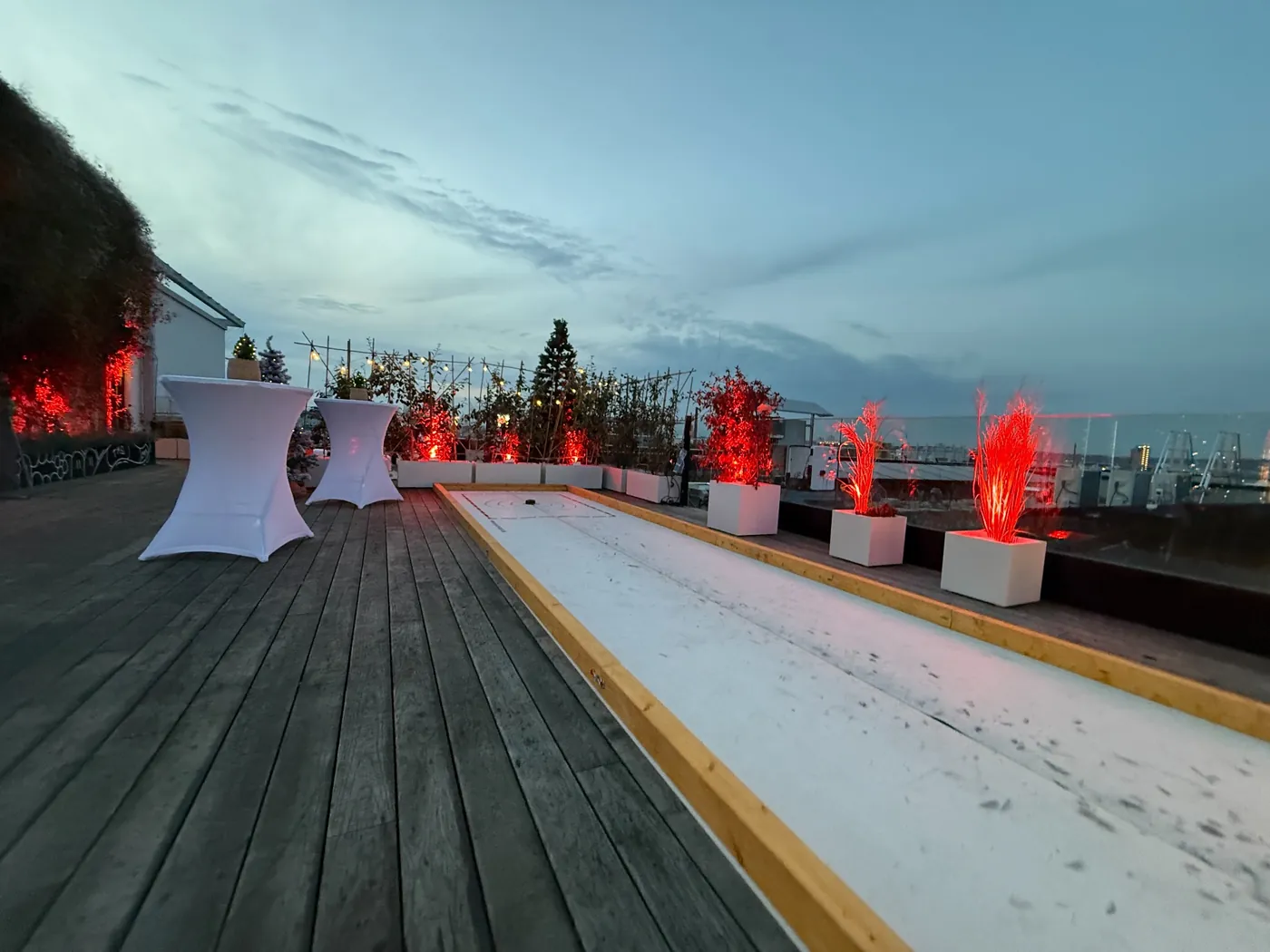 Eisstockbahn auf einer Dachterrasse bei einer Abendveranstaltung mit Stehtischen und roter Beleuchtung