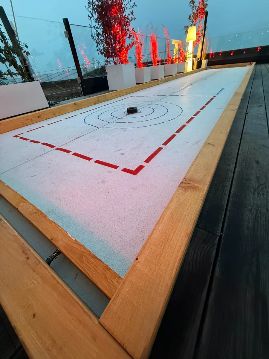 Eisstockbahn mit Holzrahmen auf einer Dachterrasse, mit Zielkreisen und roter Eventbeleuchtung