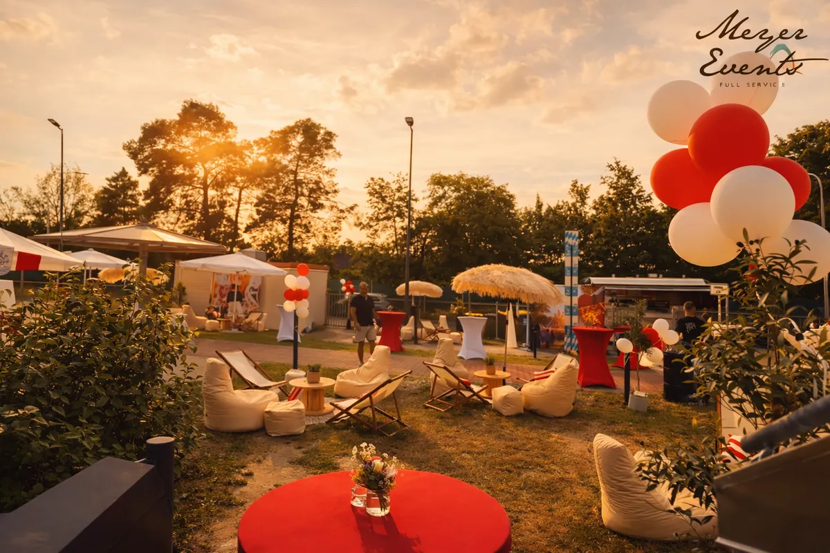 Sommerfest mit Loungemöbeln, Strohschirmen, Pflanzen und Ballons im warmen Abendlicht